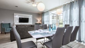 A modern dining area with a table set for six, a grey sofa, and a flat-screen TV mounted on the wall. - 1203lr Beautiful Townhome Close TO Disney (Kissimmee)