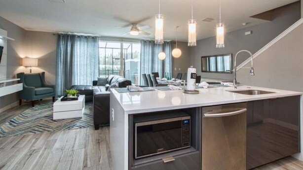 A modern kitchen with a central island, built-in microwave, and dishwasher. There is a dining area with a sofa and a lamp. - 1203lr Beautiful Townhome Close TO Disney (Kissimmee)