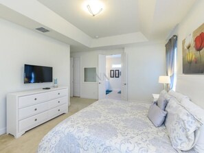 Un dormitorio con cama, televisor, cómoda y una puerta que da a otra habitación.