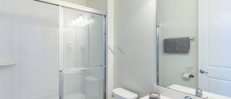 A modern bathroom with a glass shower enclosure, a white toilet, and a sink with a mirror.