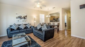 A living room with two sofas, a coffee table, and a ceiling fan. There is a dining area with a table and chairs in the background. - 1104cal 4 Bedroom Townhome in a Resort Waterpark (Bartow)