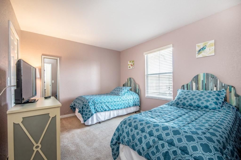 Une chambre avec deux lits, un téléviseur posé sur un meuble et une fenêtre avec des stores.