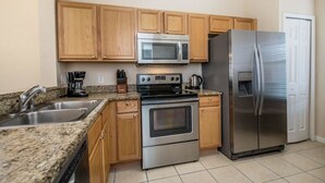 A kitchen with wooden cabinets, a stainless steel refrigerator, a microwave, an oven, and a coffee maker. - 1104cal 4 Bedroom Townhome in a Resort Waterpark (Bartow)