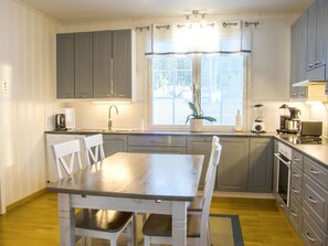 Una cocina compacta con armarios grises, una mesa de comedor de madera y una ventana con persianas.