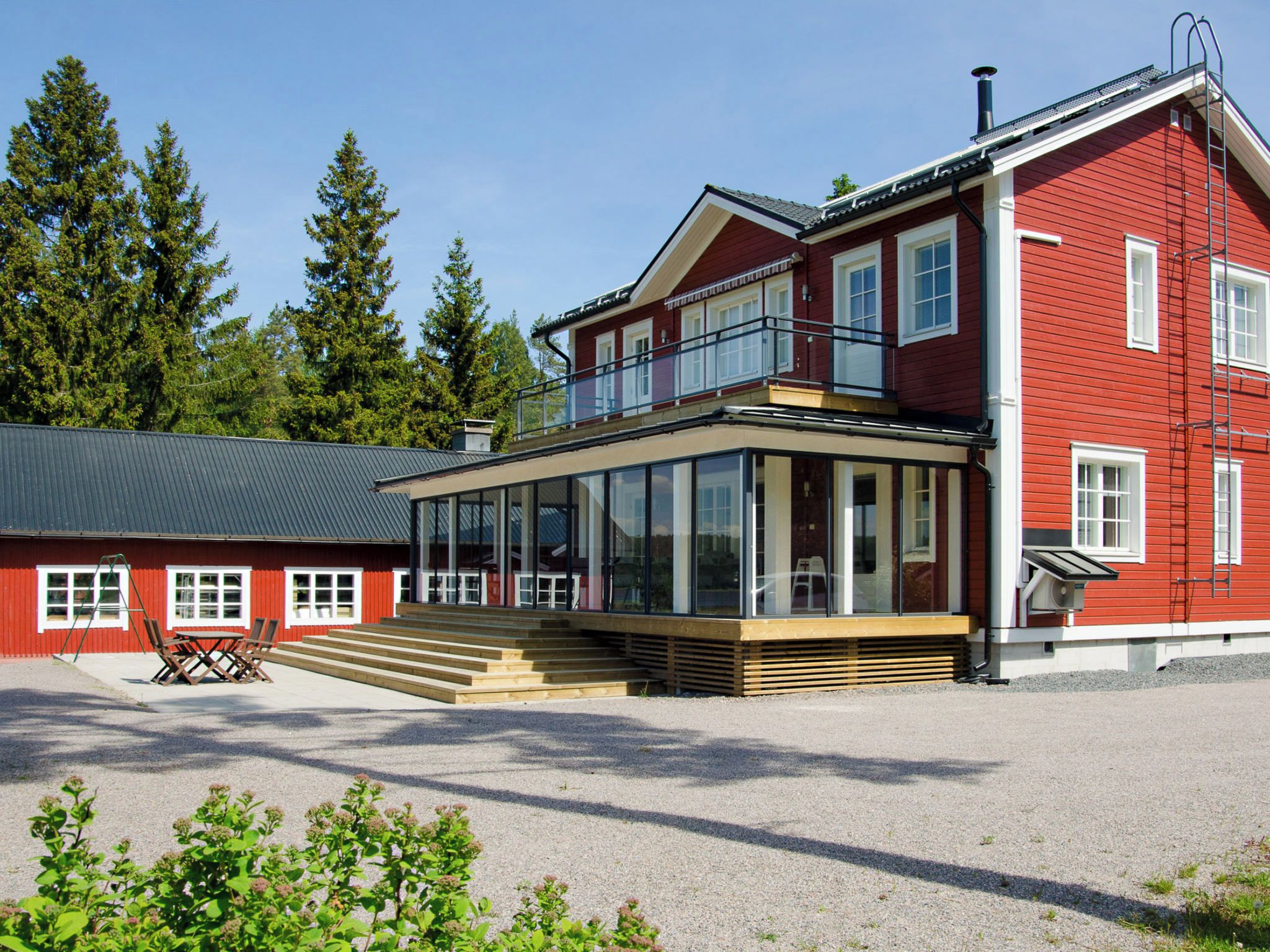 A two-story red building with a balcony, large windows, and a gravel driveway.