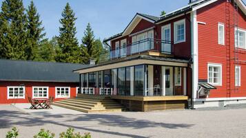 A two-story red building with a balcony, large windows, and a gravel driveway.