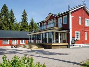 A two-story red building with a balcony, large windows, and a gravel driveway.