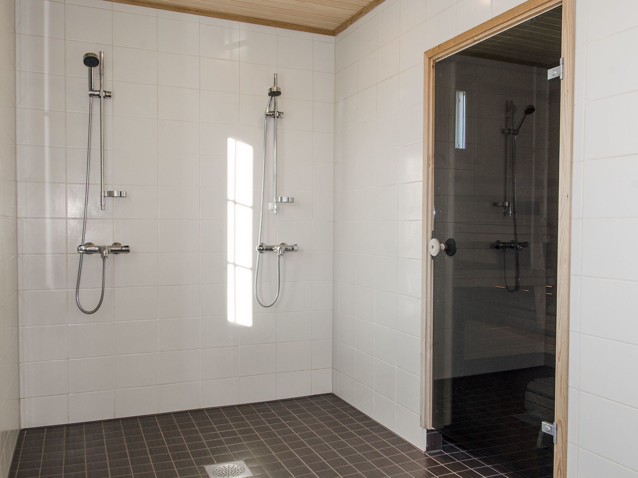 Casa de banho moderna com dois chuveiros, uma cabine de duche com portas de vidro e chão em mosaico.