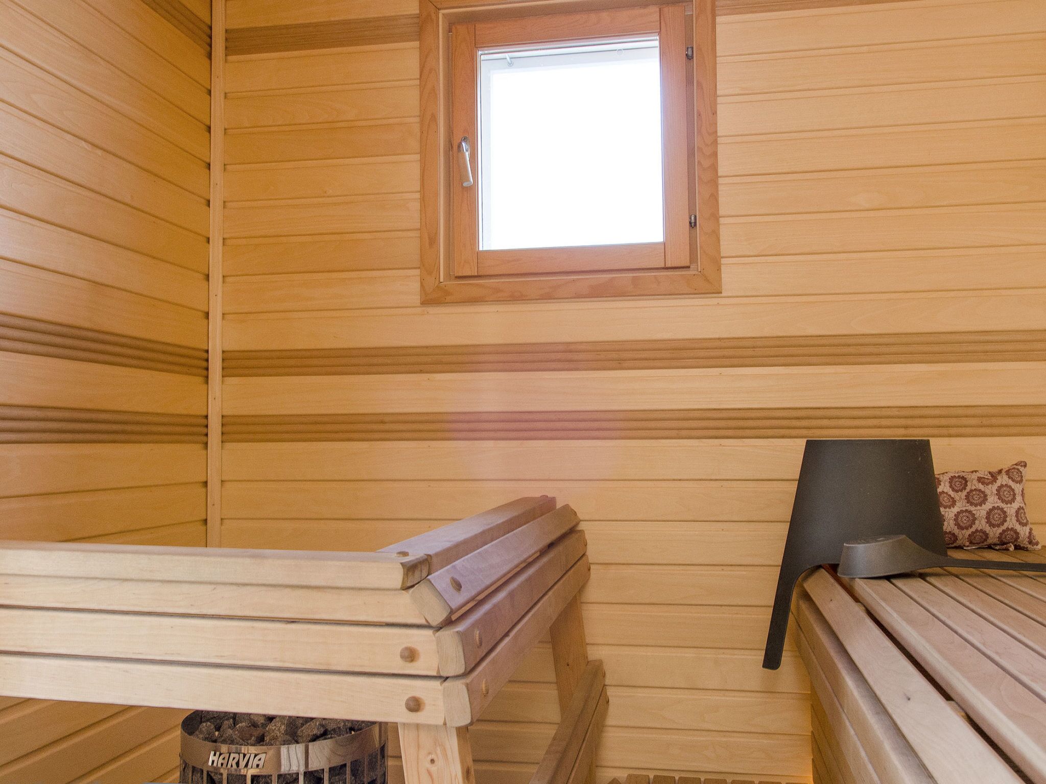 Una sala de sauna con paredes de madera, un banco, un ventanal pequeño y un banco con almohada.