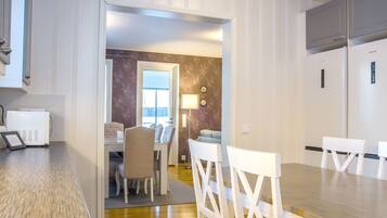 A modern kitchen with white cabinets, a built-in microwave, and a dining area with a wooden table and white chairs.