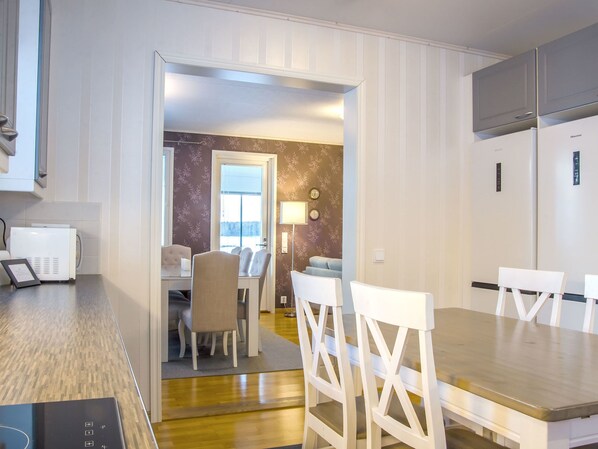 Una cocina moderna con armarios blancos, microondas integrado y un comedor con mesa de madera y sillas blancas.
