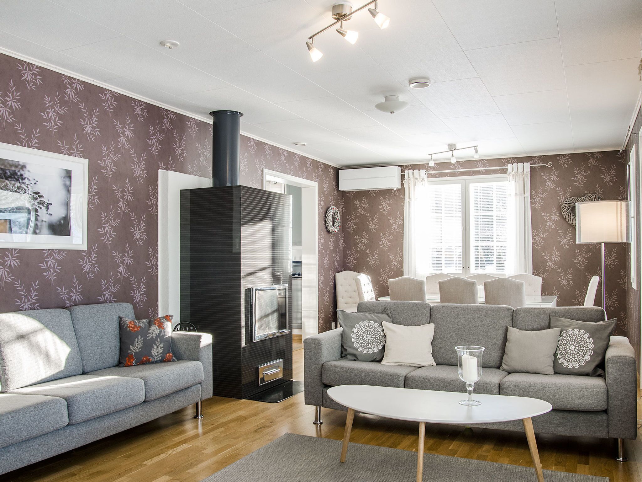 A modern living room with two grey sofas, a white coffee table, a black fireplace, and patterned wallpaper.