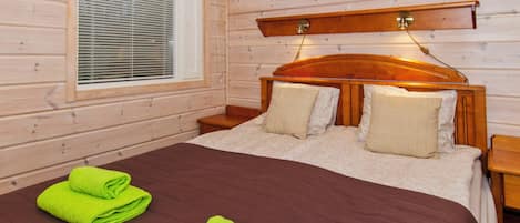 A wooden-paneled room with a bed, two pillows, a nightstand, a lamp, and a window with blinds.