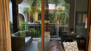 A spacious living area with a leather sofa, a dining table, and a balcony with a view of palm trees and a building. - Macaw #18 - Beach access penthouse - safe location, surfing, walking trails (Jaco)