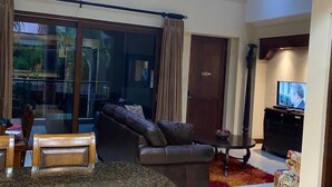 A spacious living area with a large sliding glass door leading to a balcony, a dark leather sofa, a small round table, and a television on a stand. - Macaw #18 - Beach access penthouse - safe location, surfing, walking trails (Jaco)