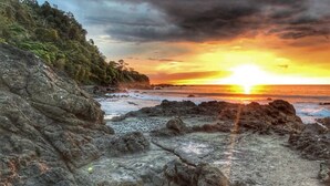 A rocky shoreline with a sunset over the ocean. - Macaw #18 - Beach access penthouse - safe location, surfing, walking trails (Jaco)