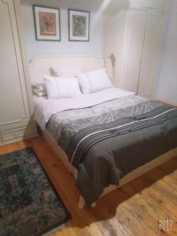 A bedroom with a bed, a nightstand, a wardrobe, and two framed pictures on the wall.