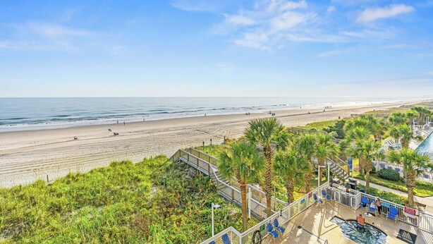 A beach view with a pool area and palm trees. - Updated Oceanfront Condo, Indoor and Outdoor Pools | Crescent Shores - N 303 (North Myrtle Beach)