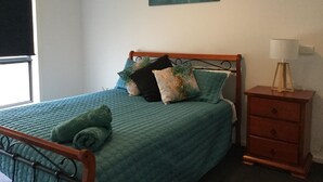 A bedroom with a bed, pillows, a bedside table, a lamp, and a painting on the wall. - AJ's Home. Modern, open plan & quiet location. (Sale)