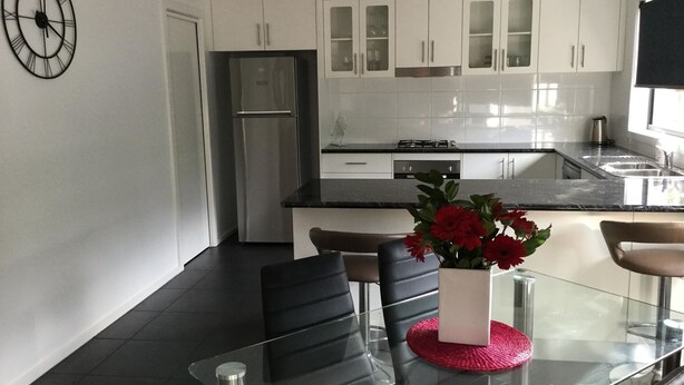 A modern kitchen with white cabinets, a stainless steel refrigerator, a glass dining table with chairs, and a clock on the wall. - AJ's Home. Modern, open plan & quiet location. (Sale)