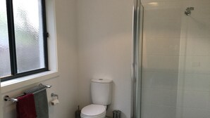 A bathroom with a toilet, a sink, a window, and a shower area. - AJ's Home. Modern, open plan & quiet location. (Sale)