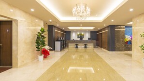 A spacious lobby with a polished marble floor, a central reception desk, and a chandelier.