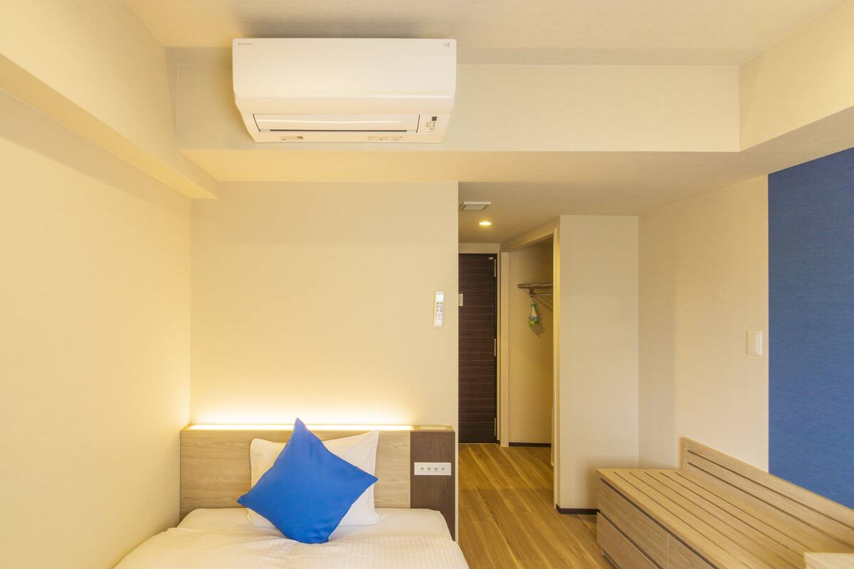 A hotel room with a bed, a bench, and an air conditioning unit.