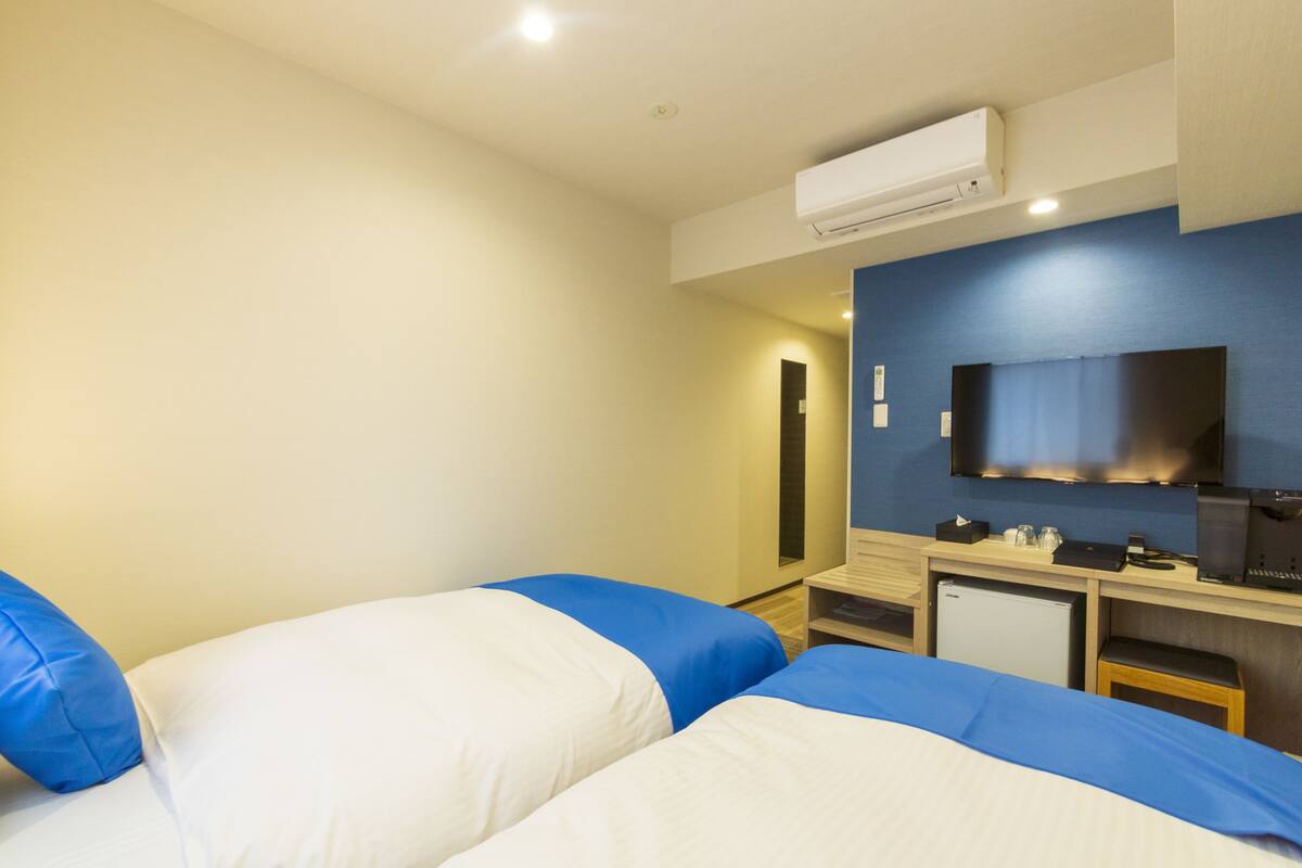 A hotel room with two beds, a desk, a television, and a small refrigerator.
