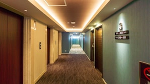 A hotel hallway with carpeted floors, wooden doors, and a ceiling with recessed lighting.