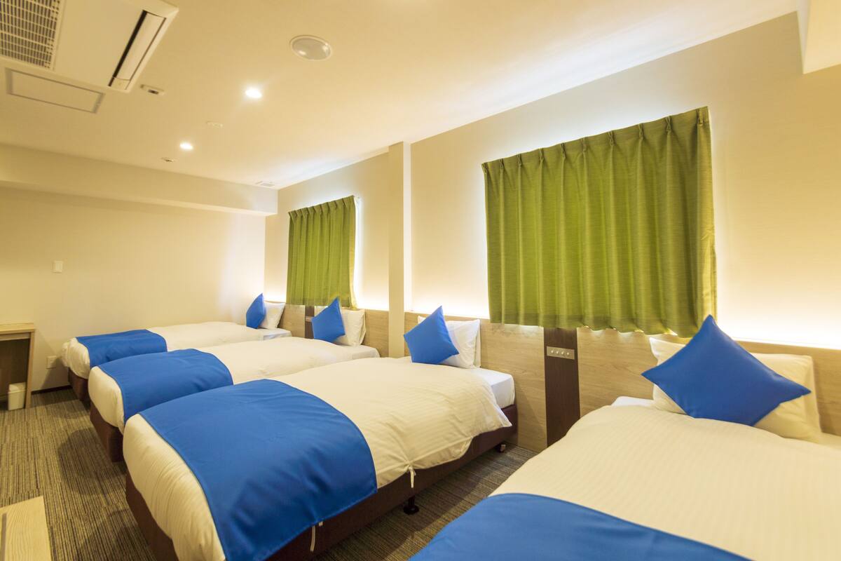 A hotel room with three beds, each with blue and white bedding, green curtains, and a wooden headboard.