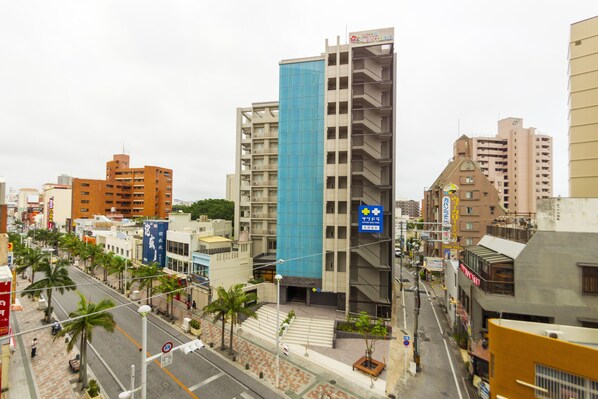 Un paisaje urbano con un edificio azul destacado, palmeras a lo largo de las calles y diversos establecimientos comerciales.