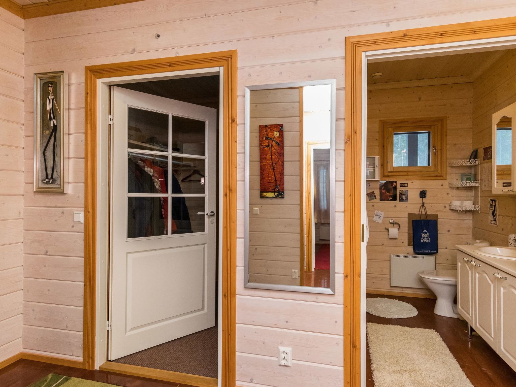 Interno di una baita in legno con un armadio, un bagno con il water e lavandino, e uno specchio.