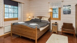 A wooden cabin bedroom with a bed, two bedside lamps, a chair, and a small table.