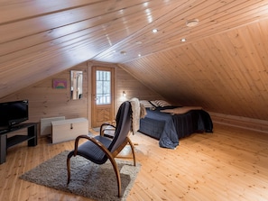 A cozy attic bedroom with wooden walls, a bed, a chair, a TV, and a dresser.