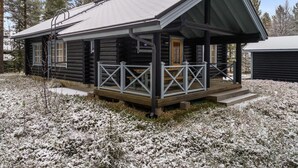 A log cabin with a porch and a covered area, surrounded by snow-covered ground and trees.