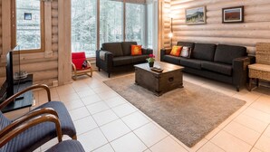 A log cabin interior with a living room, two sofas, a coffee table, and a TV.