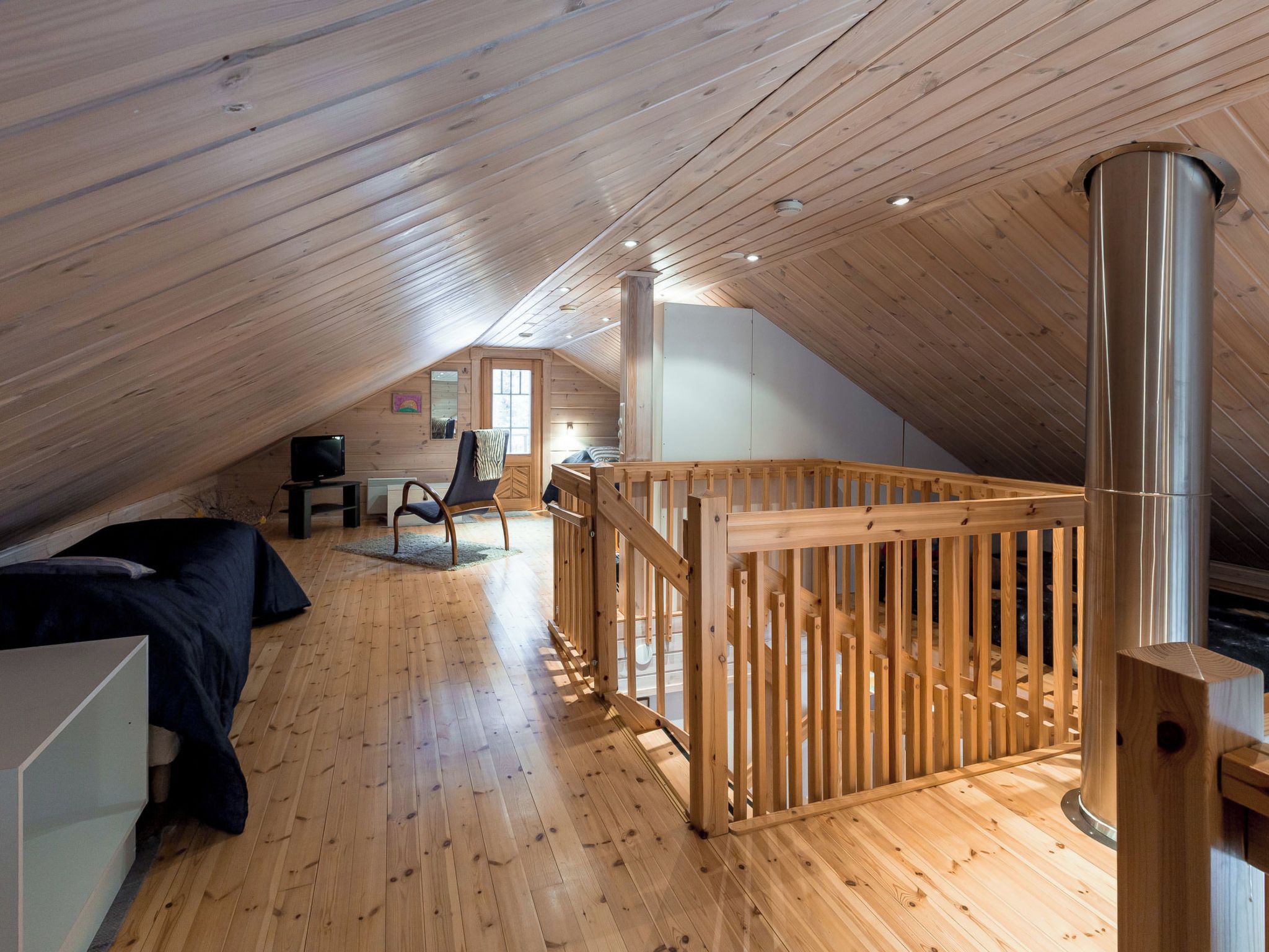 An attic bedroom with wooden floors, a bunk bed, a desk, and a chair.