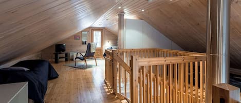 An attic bedroom with wooden floors, a bunk bed, a desk, and a chair.
