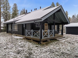 Een vakantiehuisje van hout met een veranda en schoorsteen, omringd door een met sneeuw bedekte omgeving.