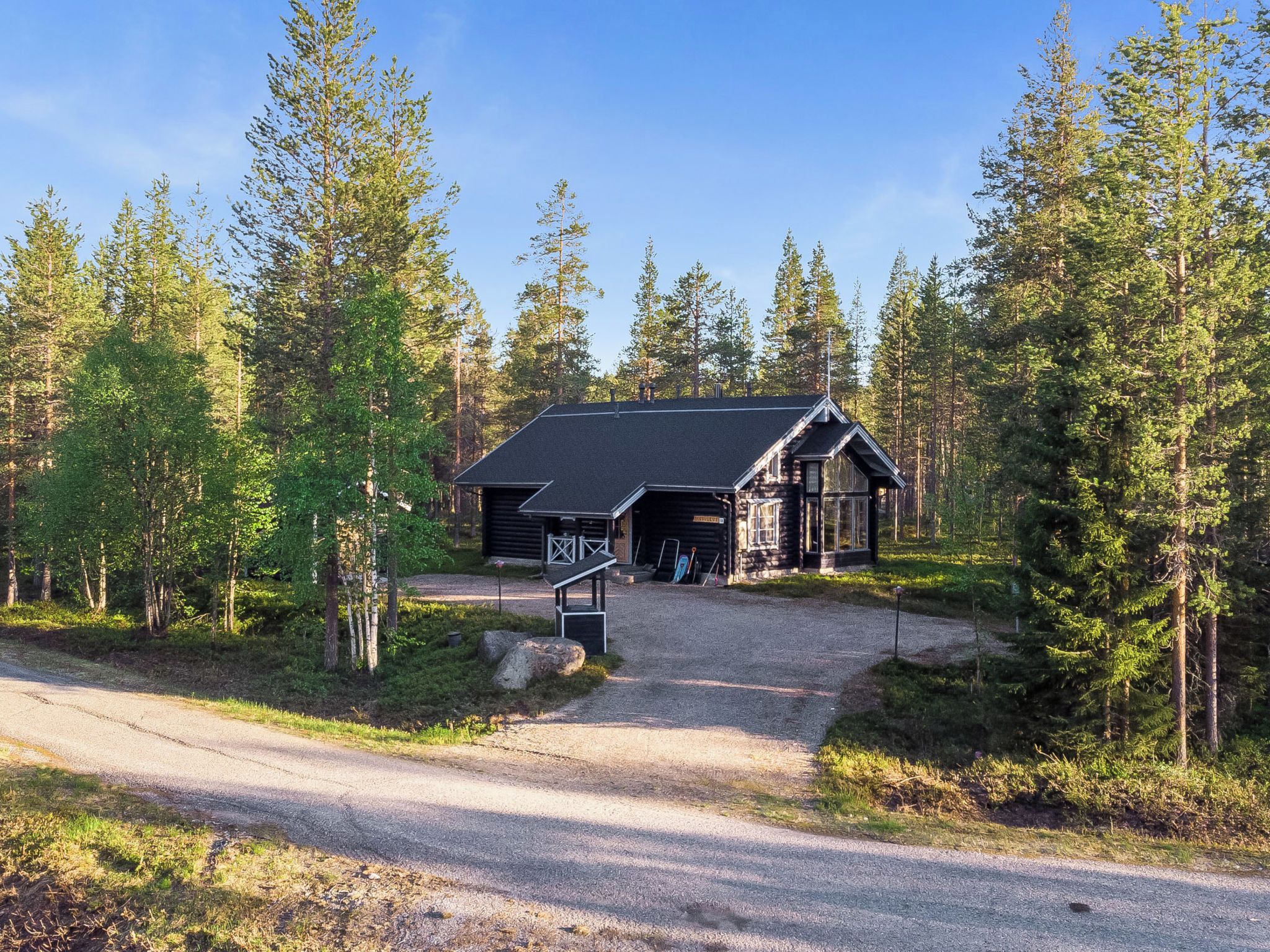 A lodge with a gravel driveway leading to a wooden building, surrounded by dense forest.