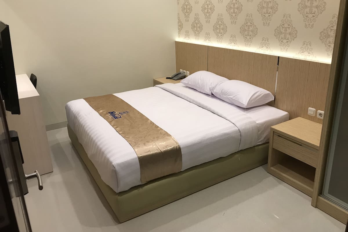 A neatly made bed with a white and gold bedspread, a bedside table with a phone, and a wall with a patterned wallpaper.