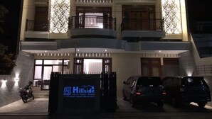 Un hotel de varios pisos con un diseño moderno, que cuenta con balcones, una entrada con portón y un cartel anunciando Hillside Suites.