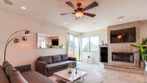 Una sala de estar moderna con sofá, mesa de centro, chimenea, televisor y ventilador de techo.