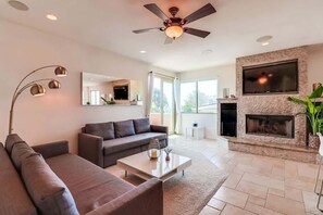 A modern living room with a sofa, coffee table, fireplace, TV, and ceiling fan.