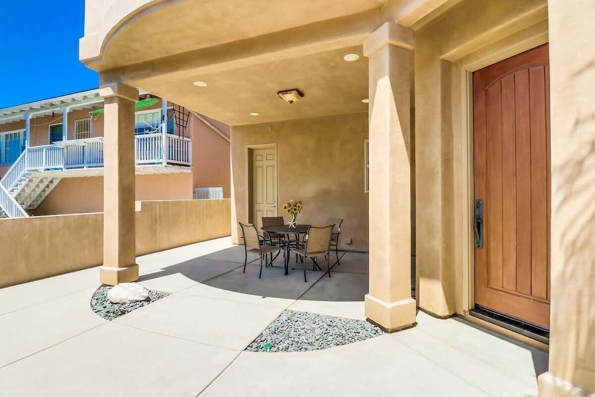 A covered patio with a table and chairs, a wooden door, and a view of a building with balconies.