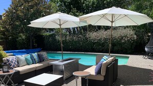 Ein Poolbereich mit Gartenmöbeln, darunter eine Sitzecke, Stühle und ein Tisch.