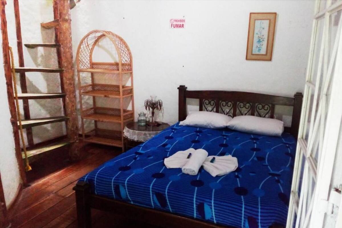 Un dormitorio con una cama, una escalera de madera, un estante y un cuadro en la pared.