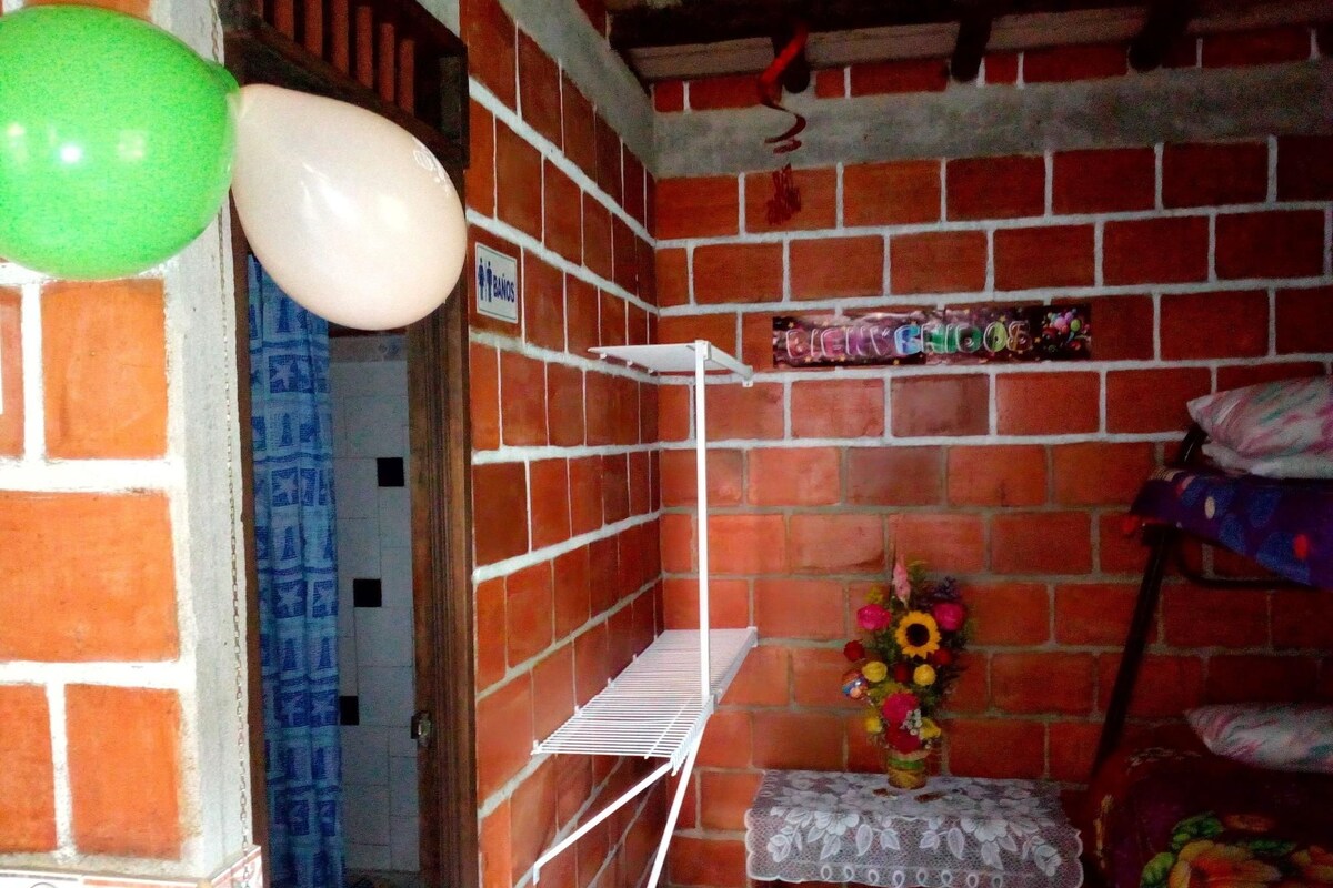A room with a brick wall, a shelf with items, a small table with a lace tablecloth, and a bouquet of flowers.