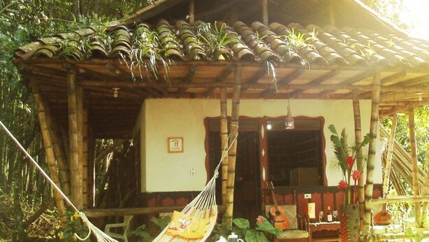 A rustic wooden house with a tiled roof, a hammock, and a small table with a teapot. - La Posada del Cucú (Salento)