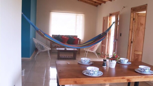 A room with a hammock, a wooden dining table with blue and white plates, and a window with a view. - Villa Cucha (Monguí)